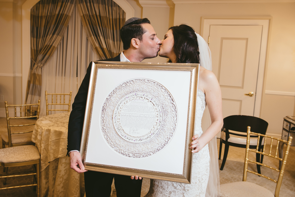 A photo of a couple holding their personalized Ketubah, featuring elements from their love story.